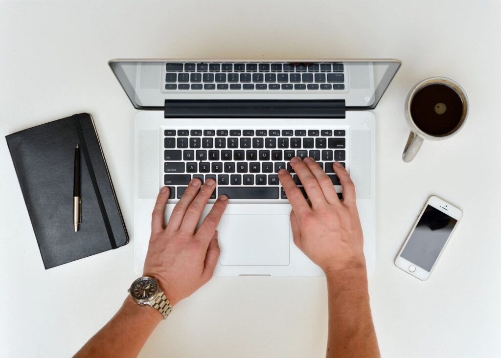 Birds eye view of hands typing on laptop with coffee, phone and notepad